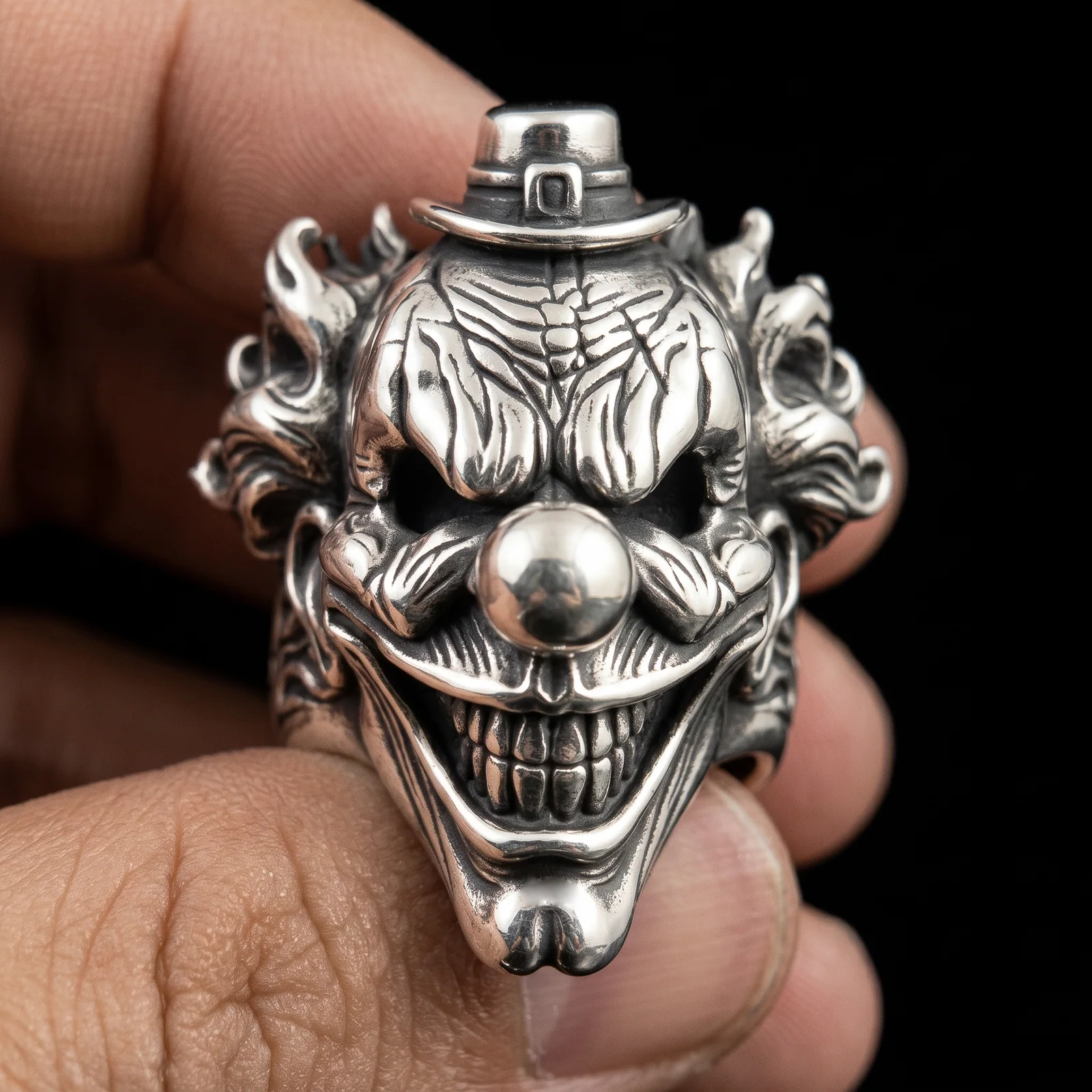 Sterling silver clown face ring held in front view with buckled hat and polished nose